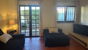 A living room with a sofa, a TV, a lamp, and a sliding glass door leading to a balcony. - Charming 3-bedroom house in Cascais perfect for your getaway (Cascais)