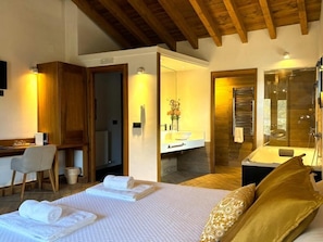 A hotel room with a bed, a desk, a chair, a bathroom, and a shower area.