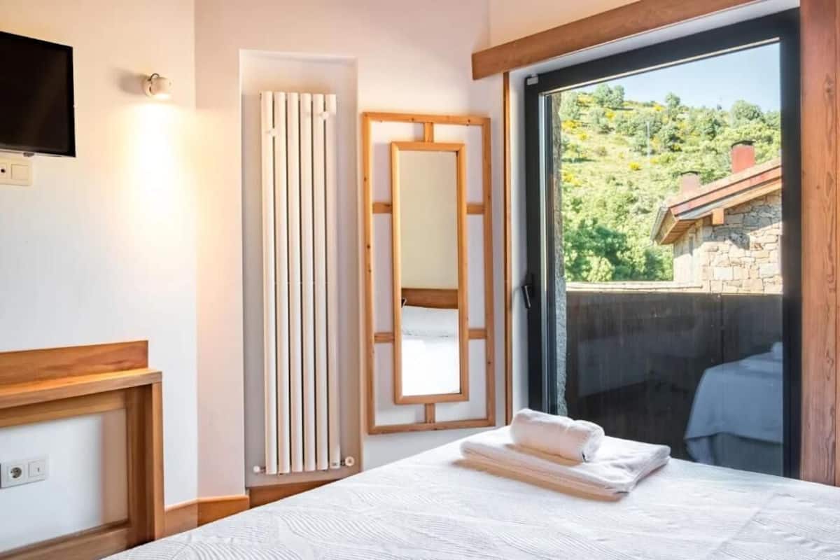 Un dormitorio con cama, un radiador, un espejo y vistas a una colina.