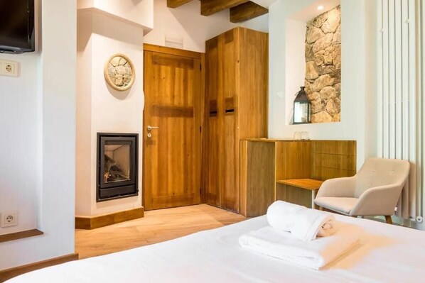 A bedroom with a bed, a wooden wardrobe, a stone wall, a fireplace, and a chair. - Hotel Gredos María Justina (San Juan de Gredos)