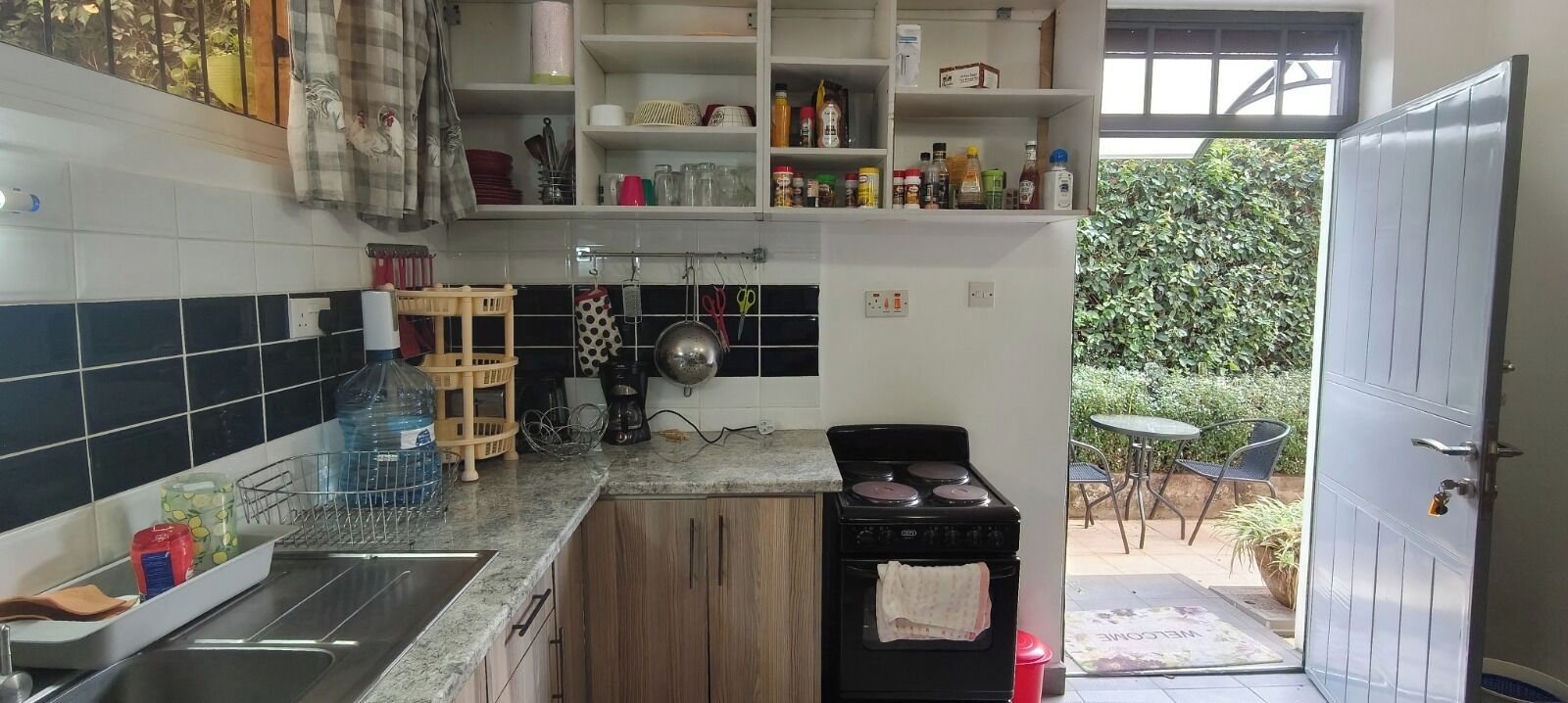 Una cocina con estufa, lavamanos y varios utensilios de cocina en estantes.