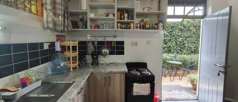Una cocina con estufa, lavamanos y varios utensilios de cocina en estantes.