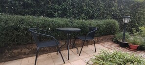 Eine Terrasse mit zwei Metallstühlen und einem kleinen, runden Tisch, umgeben von einer Hecke und Kübelpflanzen.