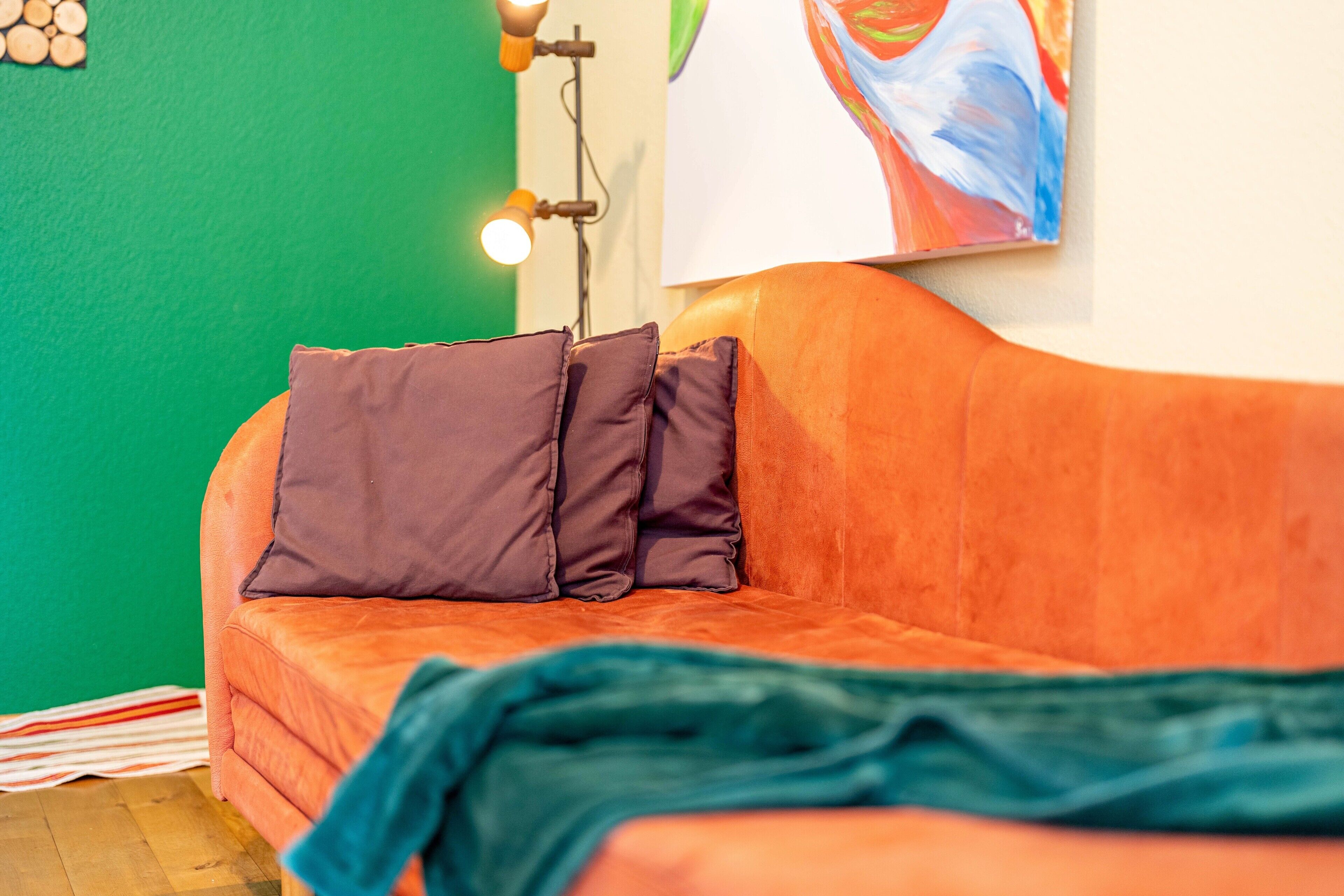 Een kamer met een groene muur, een oranje bank, een gestreept tapijt en een schilderij.