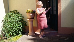Una mujer de pie frente a una puerta, con una planta en maceta a su lado.