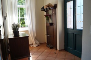 Un couloir avec une armoire en bois, une plante en pot, une porte avec un miroir et une fenêtre avec des rideaux.