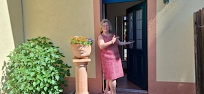 A person standing at a doorway with a potted plant beside them.