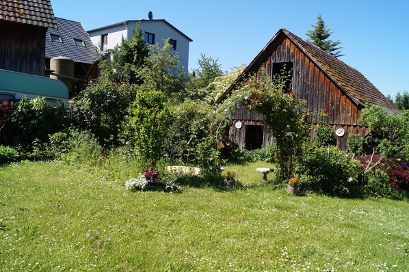 Une grange en bois rustique, entourée d’une végétation luxuriante et d’un jardin bien entretenu.