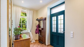 Un pasillo con un armario de madera, plantas en macetas, un perchero y una puerta color turquesa.