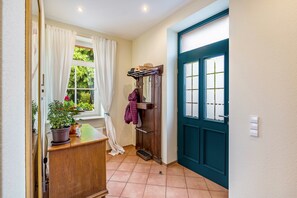 A hallway with a wooden cabinet, potted plants, a coat rack, and a teal door.