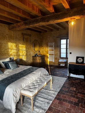 Une chambre Ă coucher comprenant un lit, un banc, une commode et une fenĂȘtre avec des volets.