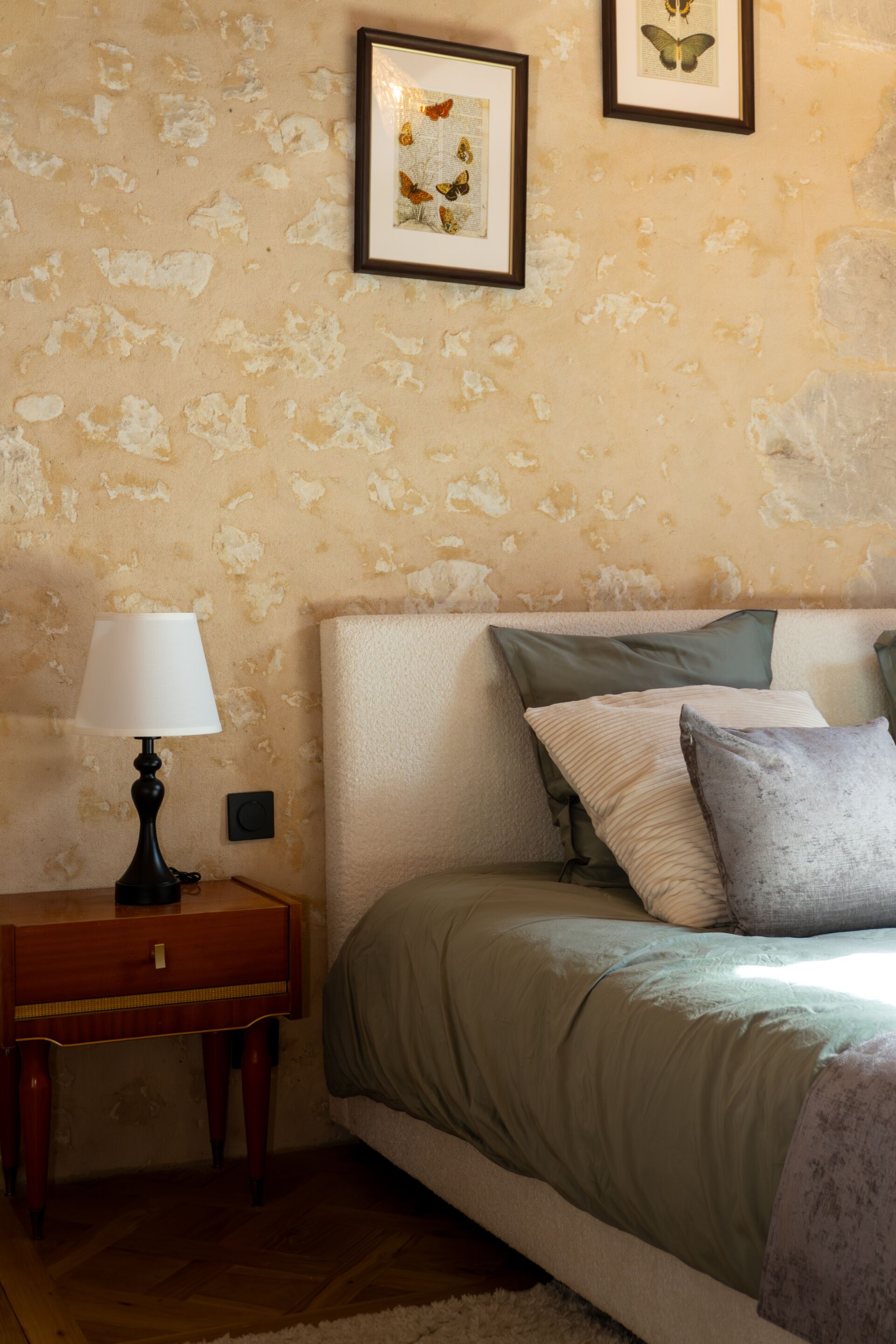 Une chambre à coucher avec un lit, des oreillers, une table de chevet, une lampe et deux tableaux encadrés accrochés au mur.