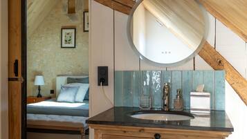 Un dormitorio con cama, mesita de noche con lámpara y espejo en la pared.