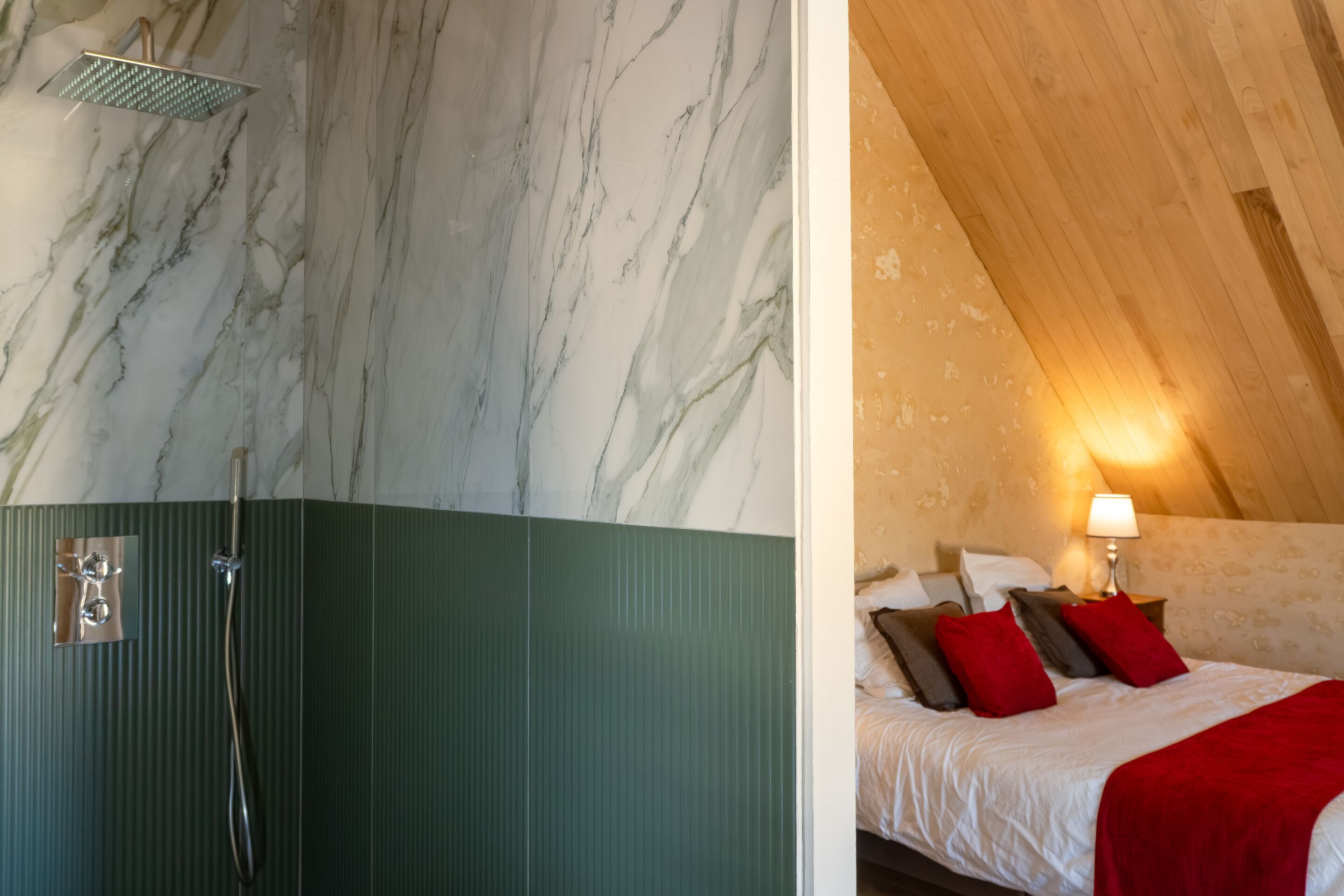 A bathroom with a shower and a bed with pillows and a lamp.