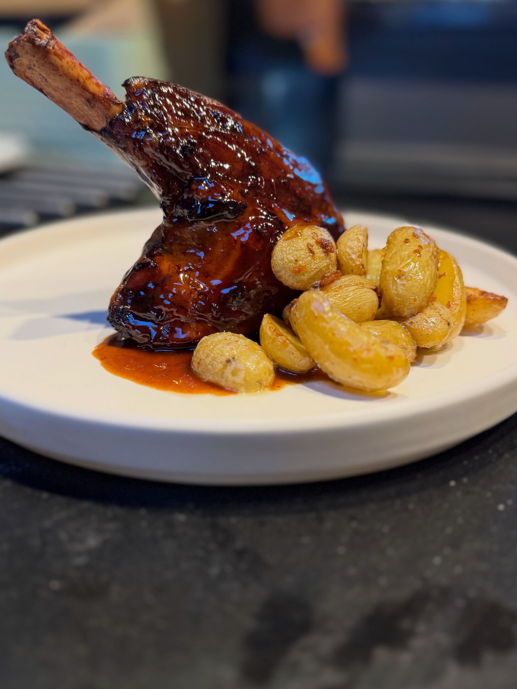 A plate with a glazed meat dish and roasted potatoes.