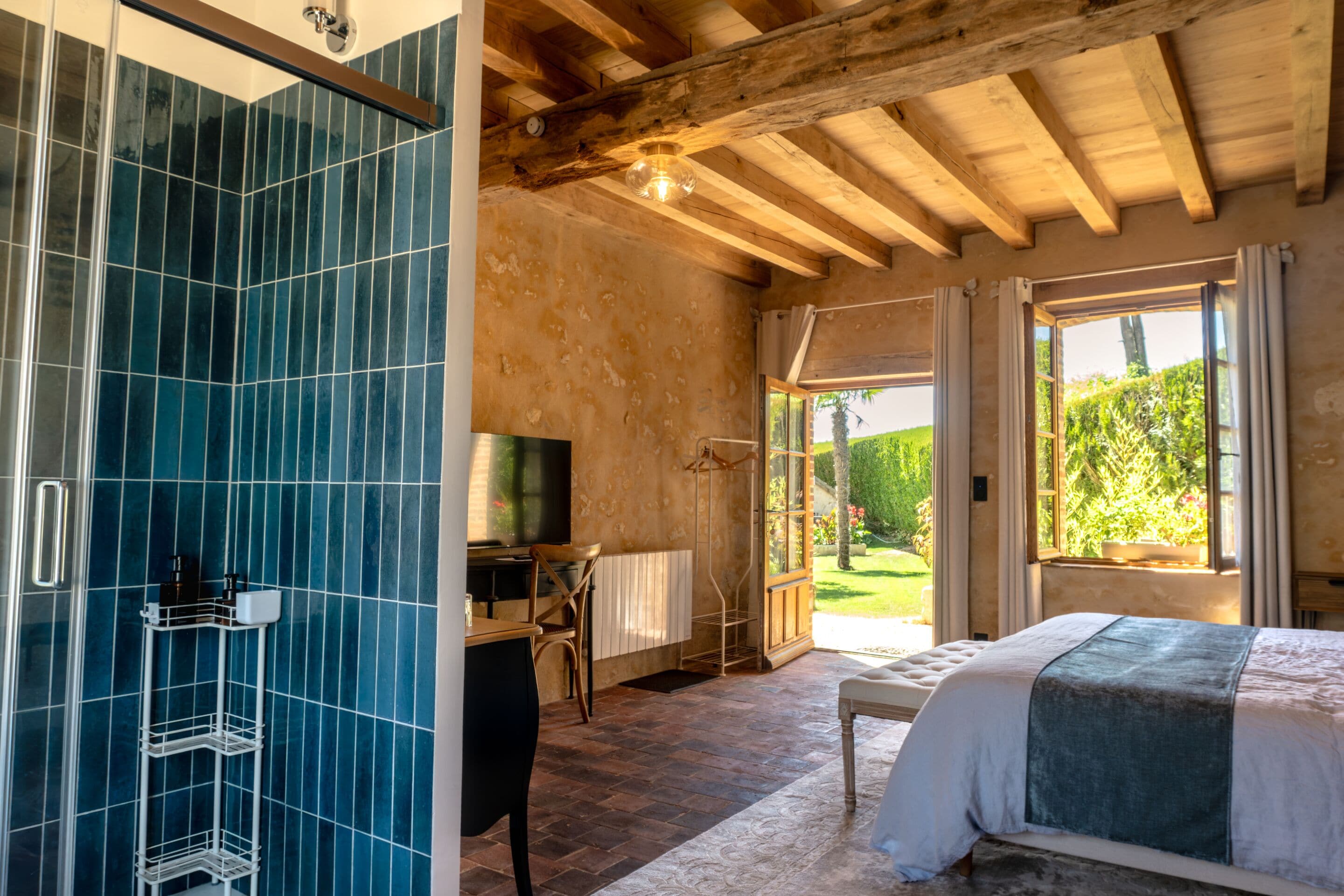 A bedroom with a large bed, a TV, a desk, and a view of the garden.