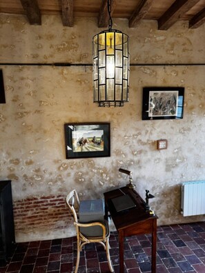 Une piÚce rustique avec des murs en briques apparentes, un plafond en bois, un luminaire suspendu, un tableau encadré, une chaise, une table et un radiateur.