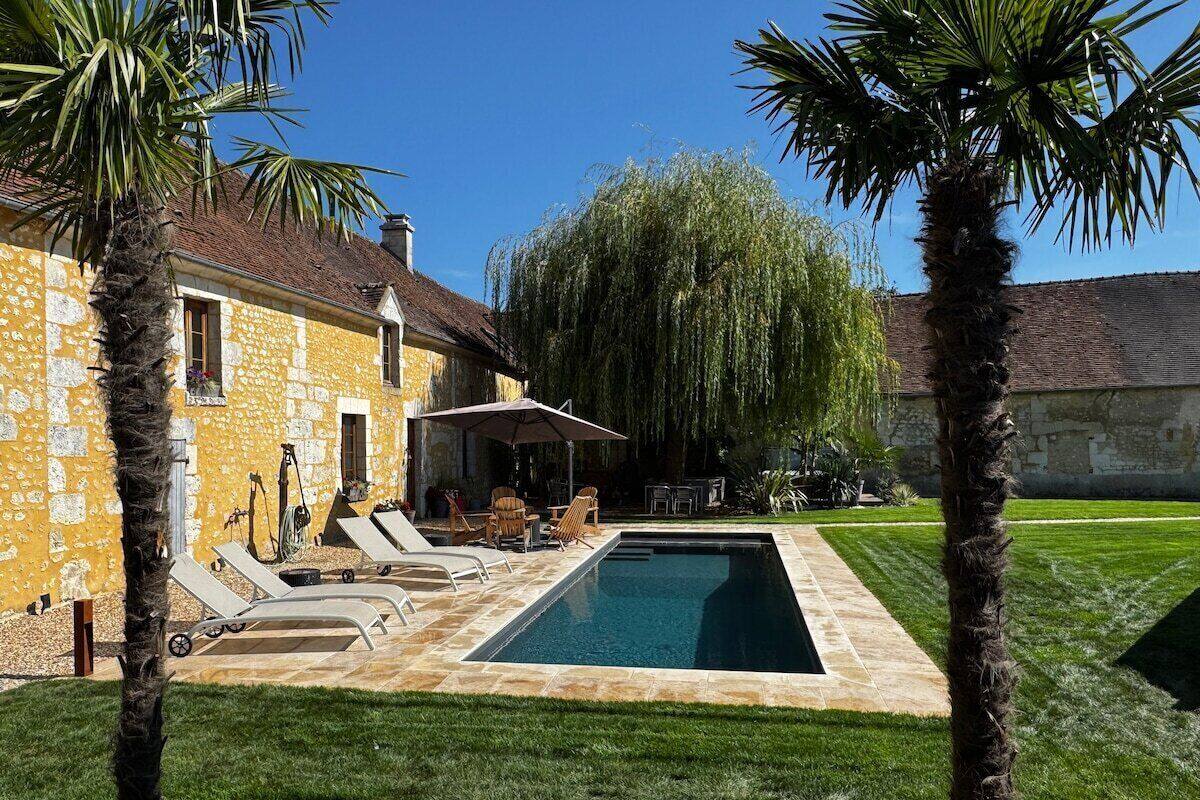 Une piscine dotée de chaises longues et d’un espace patio, le tout entouré de palmiers et bordé d’un bâtiment en pierre.