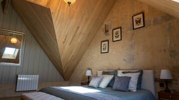 A bedroom with a sloped ceiling, a bed with multiple pillows, a bedside table with a lamp, and framed pictures on the wall.