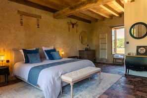 A bedroom with a large bed, a wooden headboard, a nightstand, a dresser, a mirror, and a view of the outdoors. - RELAI VALDIEU (Courgeon)