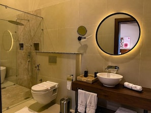 A modern bathroom with a glass-enclosed shower, a white toilet, a large round mirror, and a wooden vanity with a white sink. - Arambhaya Boutique Hotel - Kandy (Kandy)