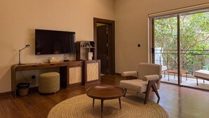 Uma sala de estar com televisão, sofá, mesa de centro, escrivaninha com computador e uma grande porta de vidro deslizante para uma varanda.