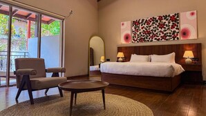 Um quarto com uma cama, uma cadeira, uma mesa redonda, um espelho grande e obras de arte na parede.