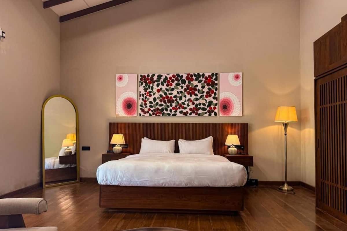 A hotel room with a large bed, two bedside lamps, a mirror, and a wall art piece.