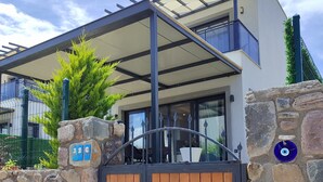 Una casa moderna con un muro in pietra, un cancello in legno e un portico coperto.