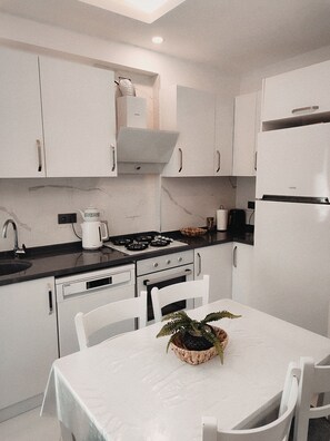 A modern kitchen with white cabinetry, a stove, a sink, and a dining table with chairs.