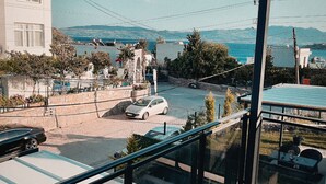 Un balcone con vista su una strada costiera, un'auto parcheggiata e un edificio con facciata bianca.