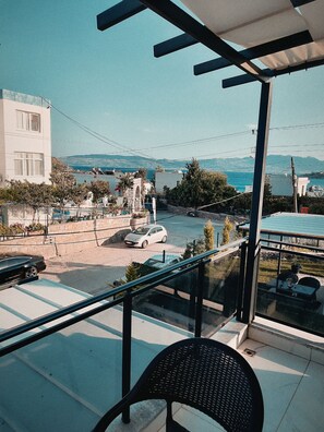 Ein Balkon mit Blick auf eine Küstenstraße, einen parkenden Wagen und ein Gebäude mit weißer Fassade.