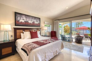 Une chambre d’hôtel avec un grand lit, un tableau au-dessus du lit, une vue sur l’extérieur grâce à une porte-fenêtre coulissante, et un espace patio avec des chaises et un parasol.