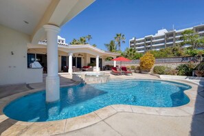 A swimming pool with a curved edge, surrounded by a patio area with outdoor furniture and a covered seating area.