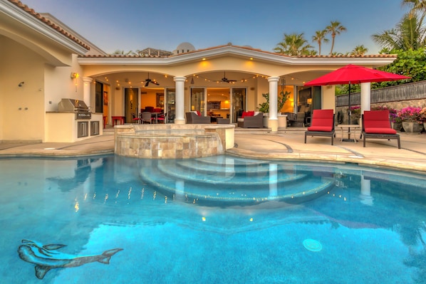 Una piscina con diseño de delfín, mobiliario exterior y una zona de terraza cubierta.