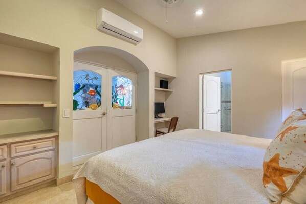 A bedroom with a bed, a desk, a chair, and a shower area.