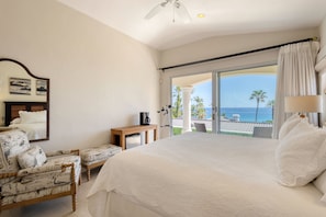 Un dormitorio con una cama grande, una silla, una mesita y vista al océano.