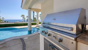 An outdoor grill with a view of the ocean and a pool.
