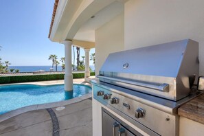 An outdoor grill with a view of the ocean and a pool.