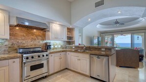 A modern kitchen with granite countertops, stainless steel appliances, and a view of the ocean through large windows.