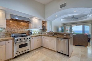 A modern kitchen with granite countertops, stainless steel appliances, and a view of the ocean through large windows.