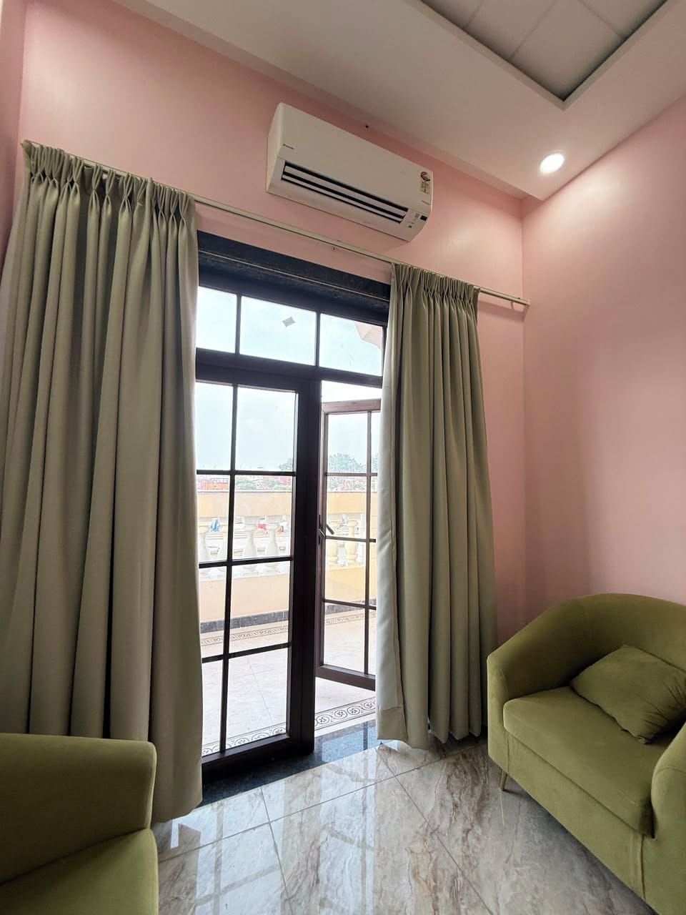 Una habitación con un ventanal grande, un equipo de aire acondicionado y un sofá verde.