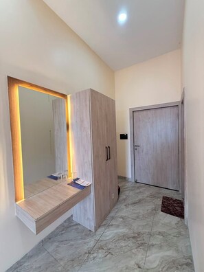 A hallway with a wooden wardrobe, a mirror with built-in lighting, a door, and a tiled floor.