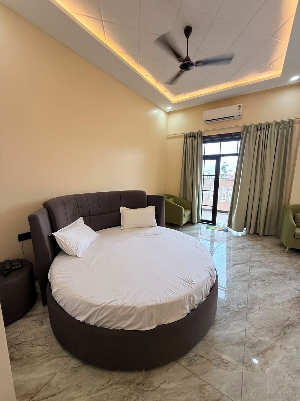 Une chambre spacieuse avec un grand lit, un ventilateur de plafond et une vue dégagée sur l’extérieur, accessible par une porte-fenêtre coulissante.