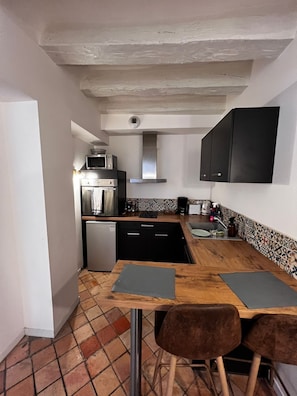 A narrow kitchen with a tiled floor, a wooden table with two chairs, and a black cabinet above the sink. - Le Rempart - Halles de Tours (Tours)