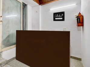 A reception area with a glass door, a reception desk, a sign reading 'Collection Company-Serviced', and a wall-mounted light fixture. - Super Collection O Sector 18 (Noida)