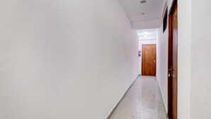 A corridor with white walls, a wooden door at the end, and a tiled floor.