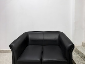A black leather armchair with a high backrest and armrests, positioned against a plain white wall. - Super Collection O Sector 18 (Noida)