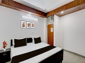 A bedroom with a bed, a nightstand, a dresser, a wall-mounted air conditioner, and framed artwork. - Super Collection O Sector 18 (Noida)