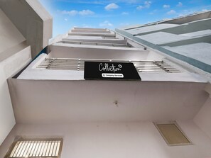 A building with a flat roof, a black sign with 'Collection' and 'Company-Serviced' text, and a small window. - Super Collection O Sector 18 (Noida)